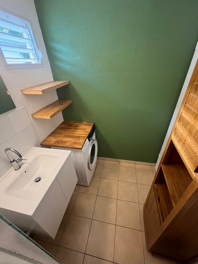 Mur vert après rénovation Salle de bain rénovée avec mur vert, étagères en bois et espace buanderie
